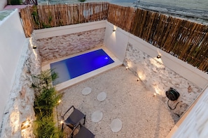 Ein kleiner Poolbereich im Freien mit einem blauen Pool, umgeben von einer Steinmauer und einem Holenzaun.