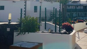En tagterrasse med pool, palmer og en hvid bygning med flere skorstene.