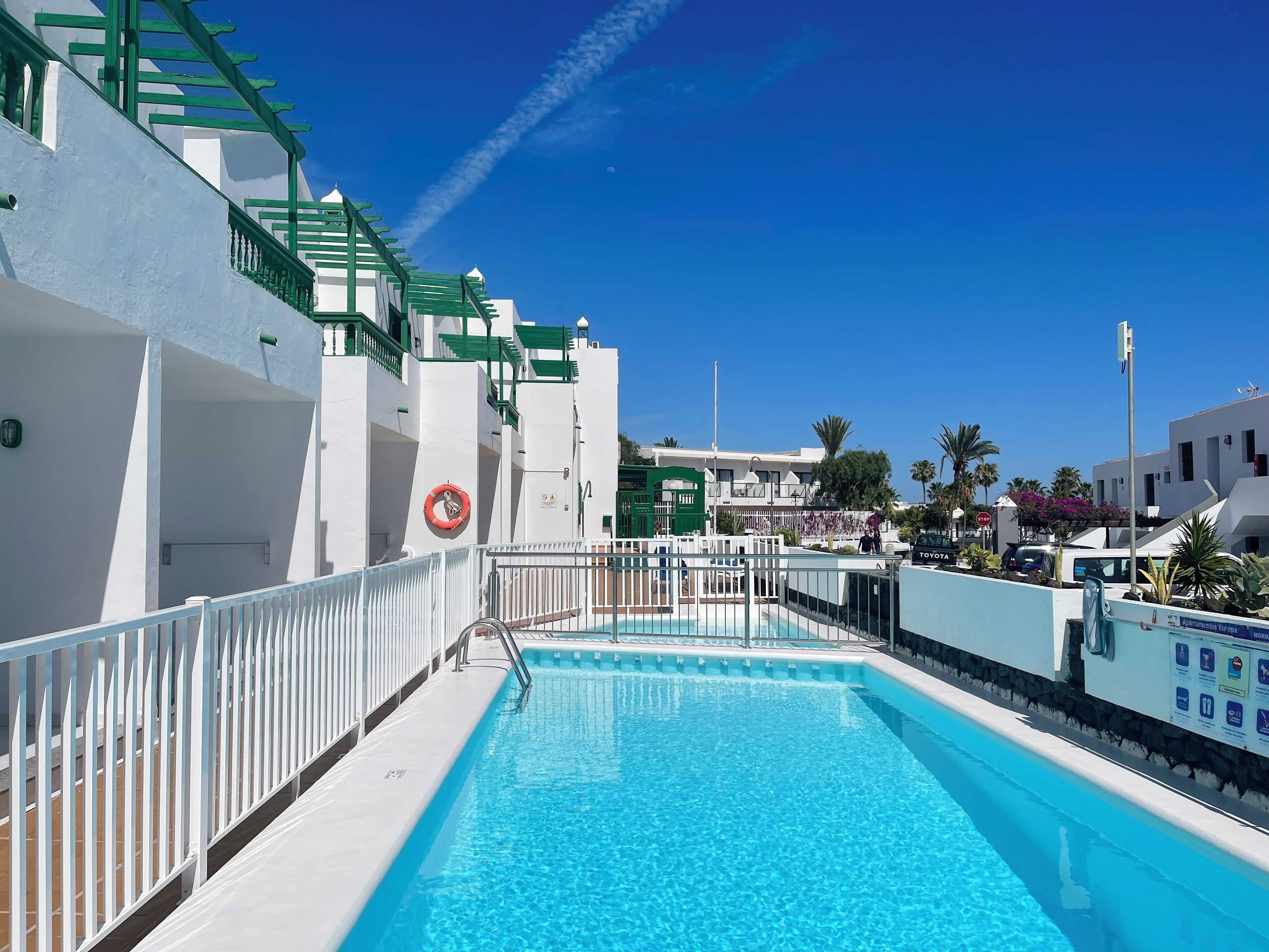 Una piscina con barandilla blanca, un flotador salvavidas y un cielo azul despejado.