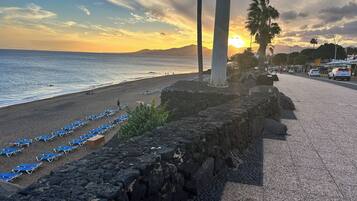 Una playa con hileras de sillas azules, un muro de piedra y una vista despejada del océano y el atardecer.