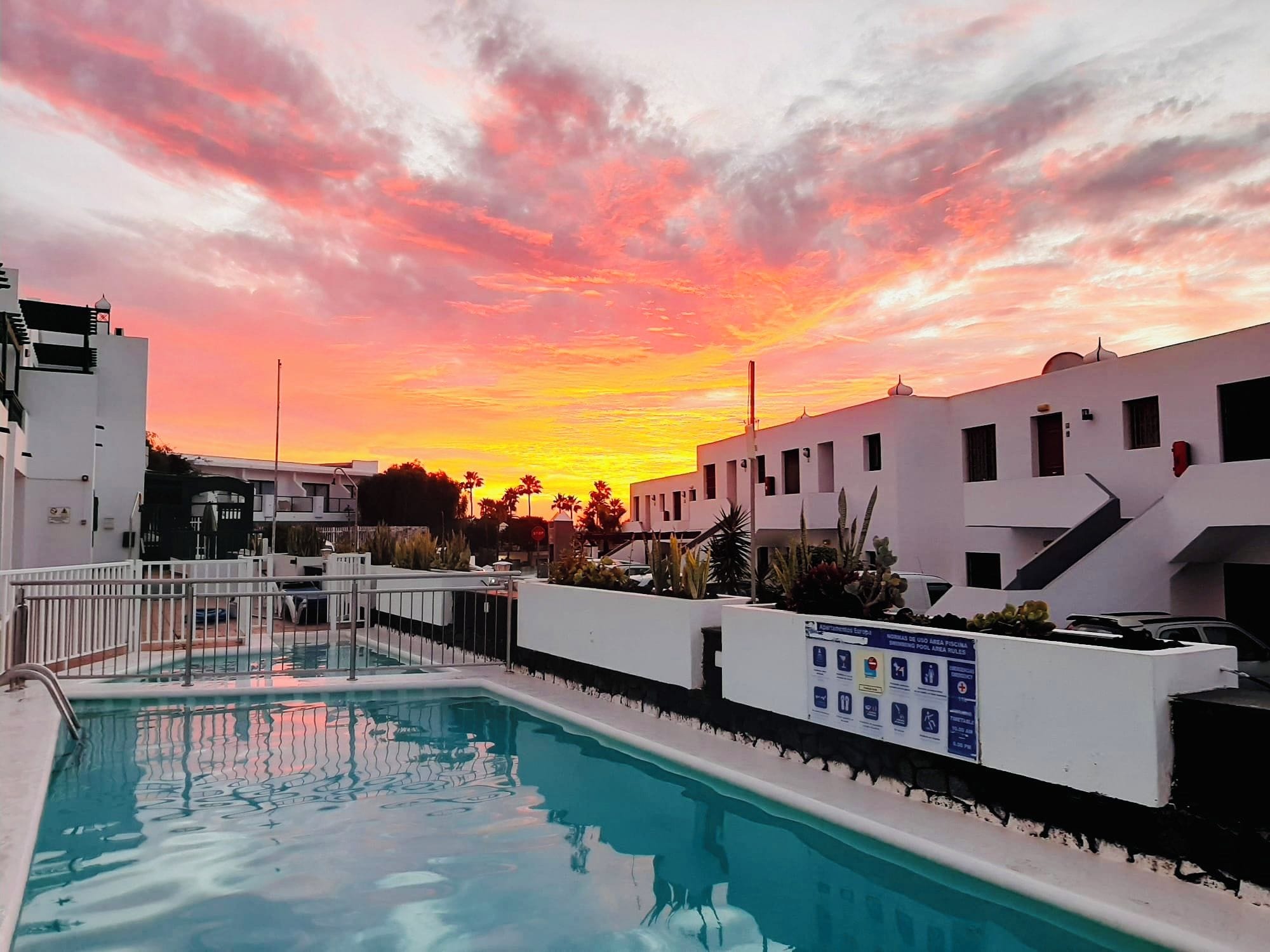 Une piscine avec vue sur le coucher de soleil, entourée de bâtiments blancs dotés de balcons.