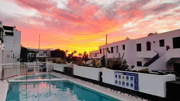 Una piscina con vista al atardecer, rodeada de edificios blancos con balcones.