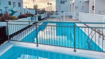 Una piscina con valla blanca, rodeada de edificios con balcones.