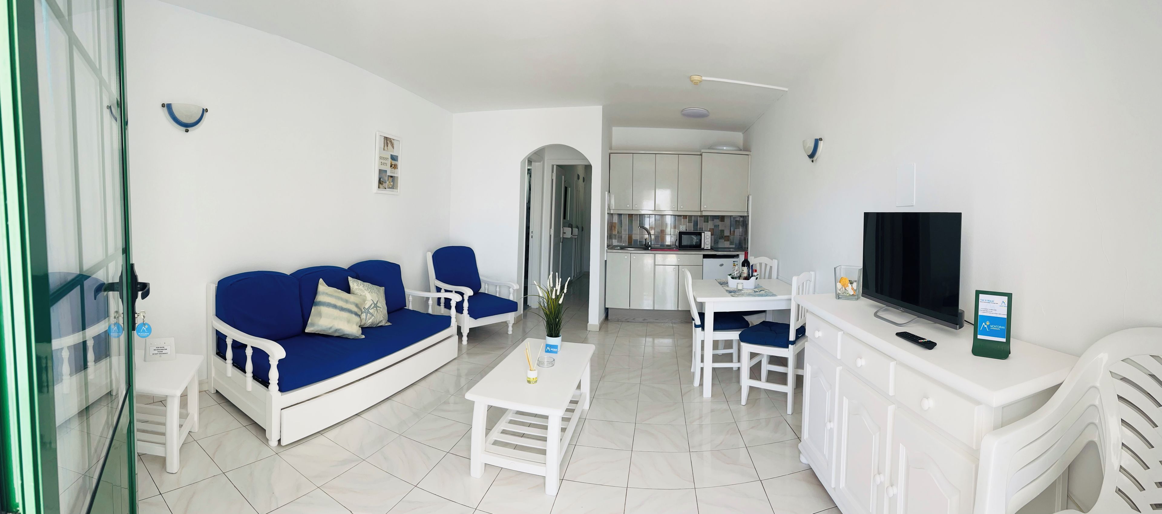 Una sala de estar moderna con sofá, sillas, una mesa de comedor, televisor y una zona de cocina.