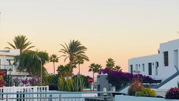 Un área de piscina con una valla blanca, palmeras y un edificio de diseño moderno.