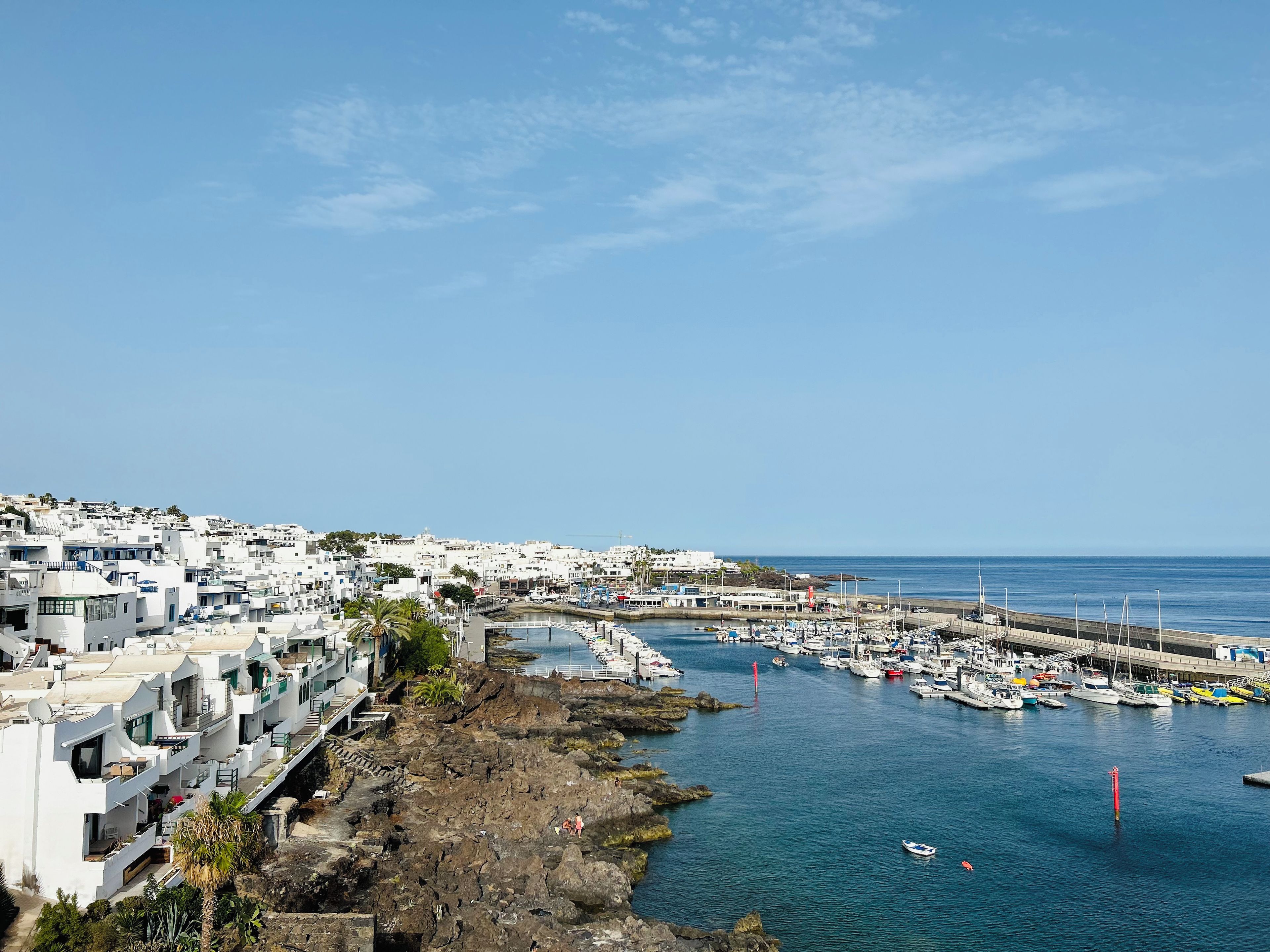 Un pueblo costero con edificios blancos, un puerto deportivo y un litoral rocoso.