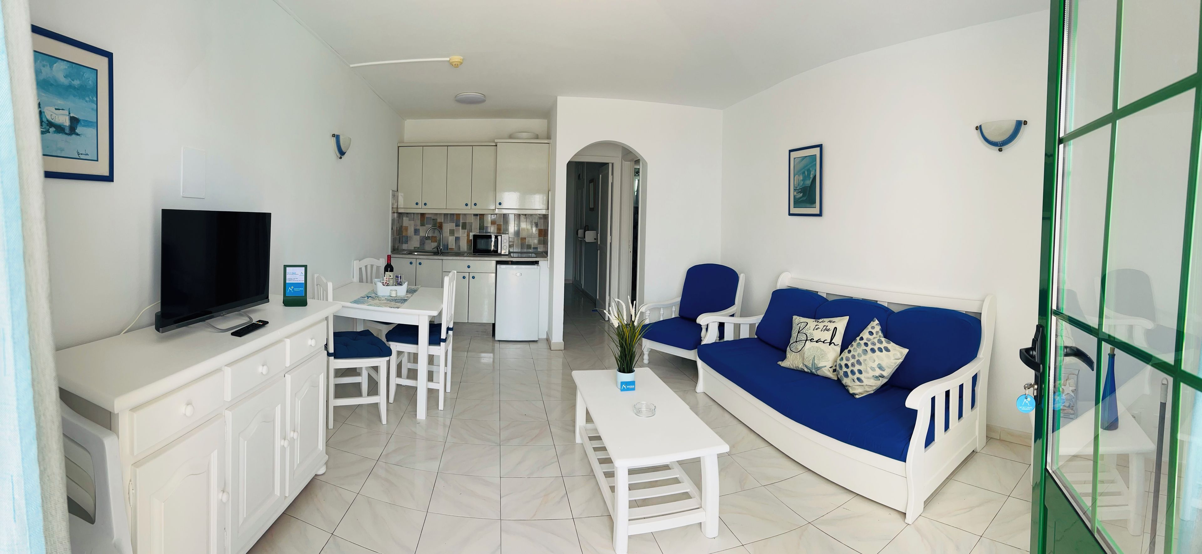 Un espacio habitable compacto con televisor, una mesa de comedor, un sofá y una kitchenette.