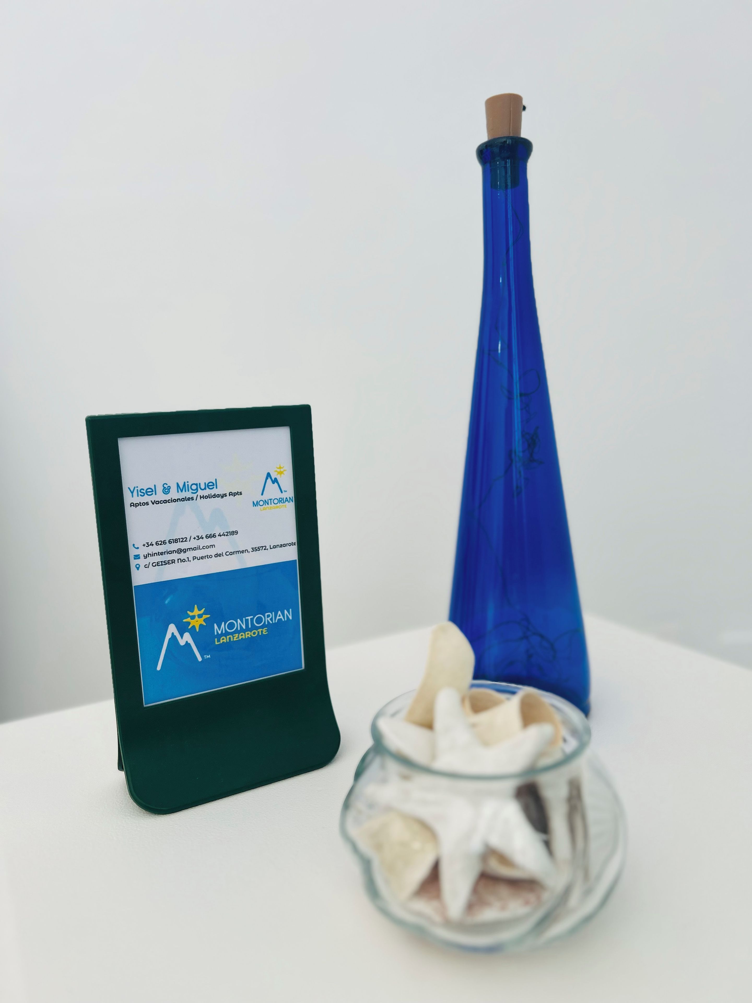 A business card for Yisel & Miguel, a company offering vacation rentals, alongside a blue bottle and a glass bowl with starfish.