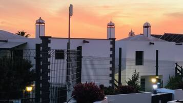 A rooftop terrace with a white building, a fence, and a sunset sky.