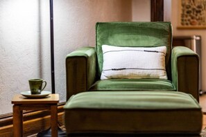 Una cadira verda amb un coixí a ratlles, una taula petita amb una tassa, i una làmpada en un racó.