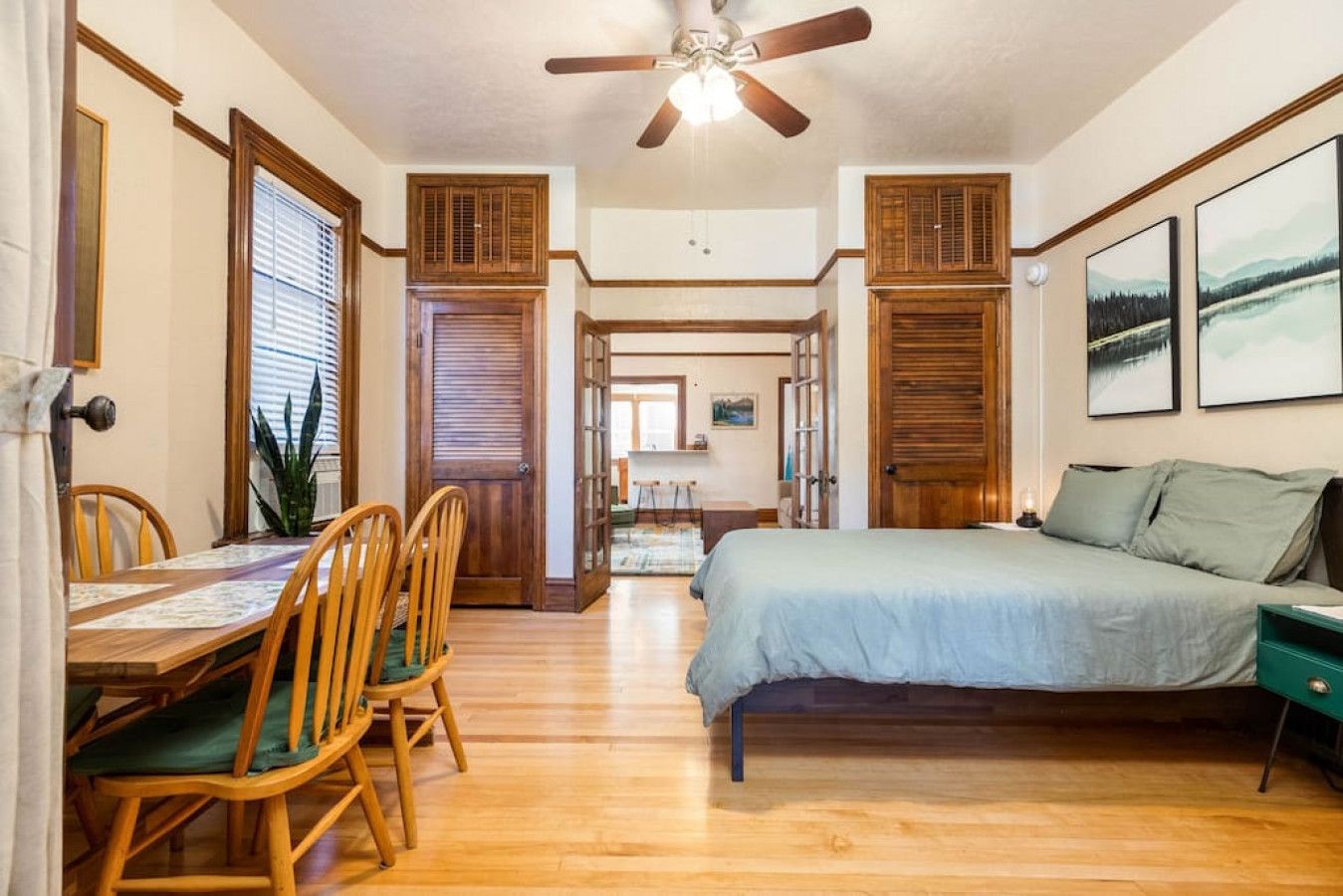 A room with a bed, a dining table with chairs, and a ceiling fan.