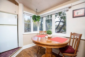 A dining area with a wooden table, two chairs, a hanging plant, and a window with a view of trees. - AEA Historic Avenues - 195 F St. SLC   (Salt Lake City)