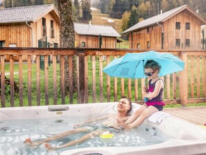 A hot tub with a wooden deck and a person lying inside. - One-bedroom Cabin (Sankt Georgen am Kreischberg)