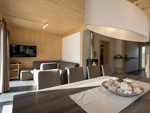 A modern living room with a flat-screen TV, a fireplace, and a dining area with a table set for four. - One-bedroom Cabin (Sankt Georgen am Kreischberg)