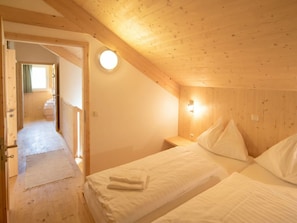 Ein Zimmer mit zwei Betten, einer Holzbalkendecke, einer runden Lampenleuchte und einem sichtbaren Badezimmer im Hintergrund.
