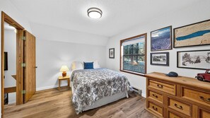 A bedroom with a bed, a nightstand, a dresser, and a window with a view. - Pines & Peace by Avantstay Log Cabin + Wraparound Deck + Grill Mins to Ski & Lake (Truckee)