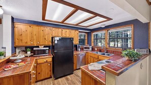 A kitchen with wooden cabinets, a black refrigerator, a microwave, a toaster, and a sink. - Pines & Peace by Avantstay Log Cabin + Wraparound Deck + Grill Mins to Ski & Lake (Truckee)