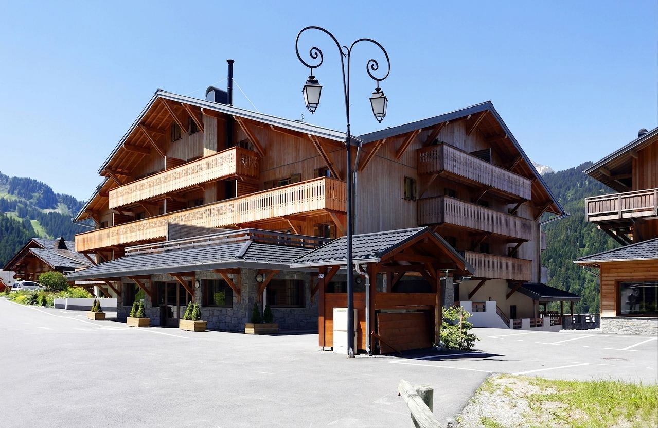 Ein mehrstöckiges Holzgebäude mit Balkonen, einem gepflasterten Parkplatz und einem Berg im Hintergrund.