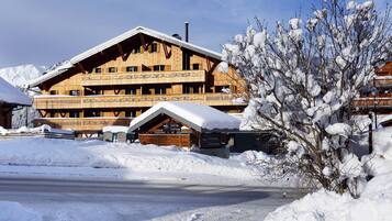 Ein mehrstöckiges Holzchalet mit Balkonen, umgeben von verschneitem Gelände und Bergen im Hintergrund.