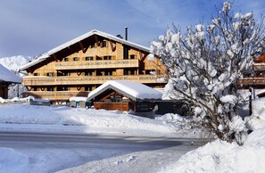 Un chalet en bois à plusieurs étages, doté de balcons, entouré d’un paysage enneigé et avec des montagnes en arrière-plan.