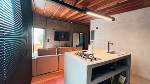 Eine moderne Küche mit eingebautem Gasherd, einer Spüle und einer Arbeitsplatte. Das Zimmer verfügt über eine Holzbalkendecke und ein großes Fenster mit Jalousien.