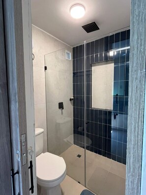 Ein modernes Badezimmer mit Duschkabine aus Glas, einer weißen Toilette und einem Spiegel an der Wand.