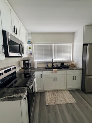 A modern kitchen with white cabinetry, a stainless steel refrigerator, and a built-in oven.