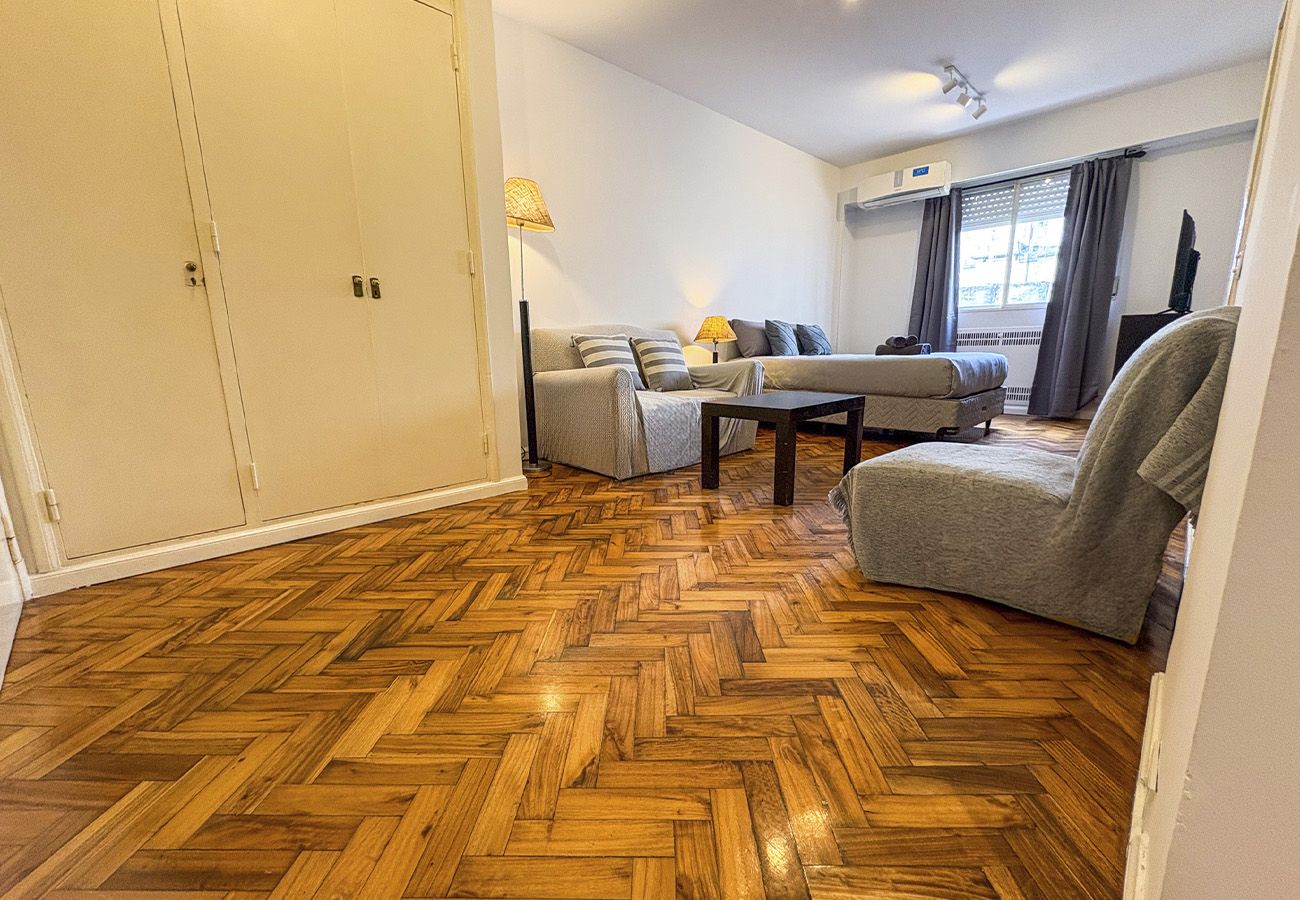 Une pièce avec un parquet en point de Hongrie, un ensemble de canapés, un fauteuil et un téléviseur.