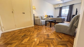 A room with a herringbone wooden floor, a sofa set, a chair, and a television.