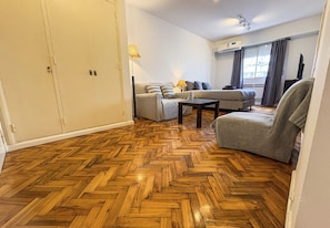 Una habitación con piso de madera tipo espiga, un conjunto de sofá, un sillón y un televisor.