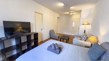 Una habitación de hotel con una cama, televisión, escritorio, silla y lámpara.