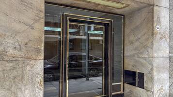 Puerta de ascensor de vidrio con marco metálico, ubicada en un edificio con paredes de mármol.