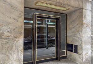 Puerta de ascensor de vidrio con marco metálico, ubicada en un edificio con paredes de mármol.