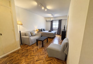 Un espacio habitable compacto con un sofá, un sillón, una mesita de centro y una cama.