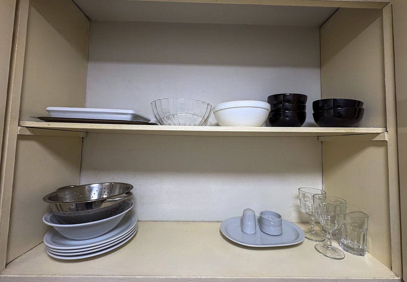 Una cocina con dos estantes; el estante superior tiene cuencos y platos, y el estante inferior tiene una pila de platos y un colador.
