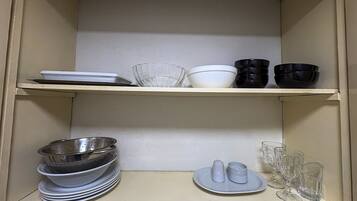 Una cocina con dos estantes; el estante superior tiene cuencos y platos, y el estante inferior tiene una pila de platos y un colador.