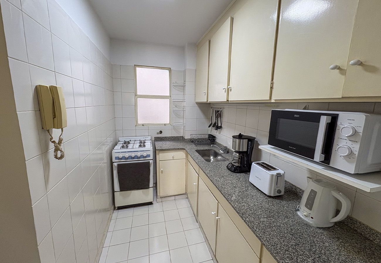 Una cocina compacta con gabinetes blancos, estufa, microondas, tostadora y hervidor.