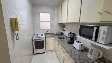 Una cocina compacta con gabinetes blancos, estufa, microondas, tostadora y hervidor.