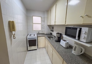 Una cocina compacta con gabinetes blancos, estufa, microondas, tostadora y hervidor.
