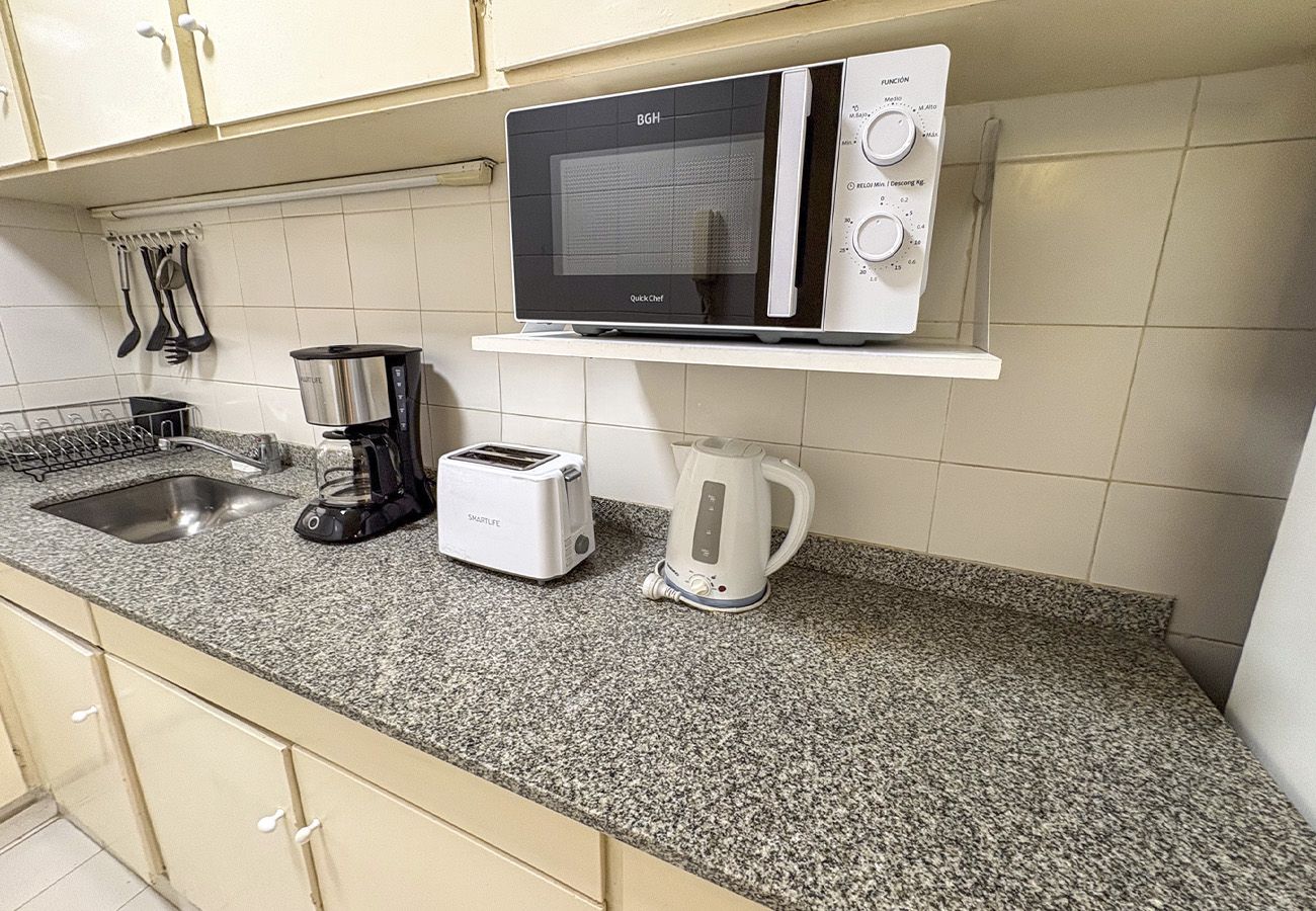 A kitchen with a microwave, toaster, kettle, and coffee maker on a granite countertop.