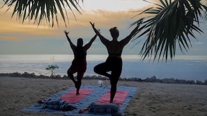 Two individuals practicing yoga on a beach with a view of the ocean.