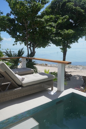 A poolside area with lounge chairs, a wooden deck, and a view of the sea.