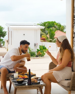 A couple dining outdoors with a table set for two, surrounded by greenery and a white building in the background. - Ix Chel Wellness Resort (San Pedro)
