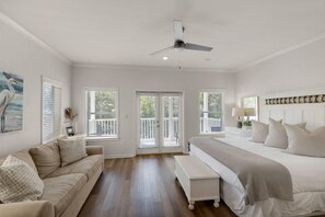 A bedroom with a large bed, a sofa, a ceiling fan, and a view of the outdoors through the windows. - Seabreeze 30A (Panama City Beach)