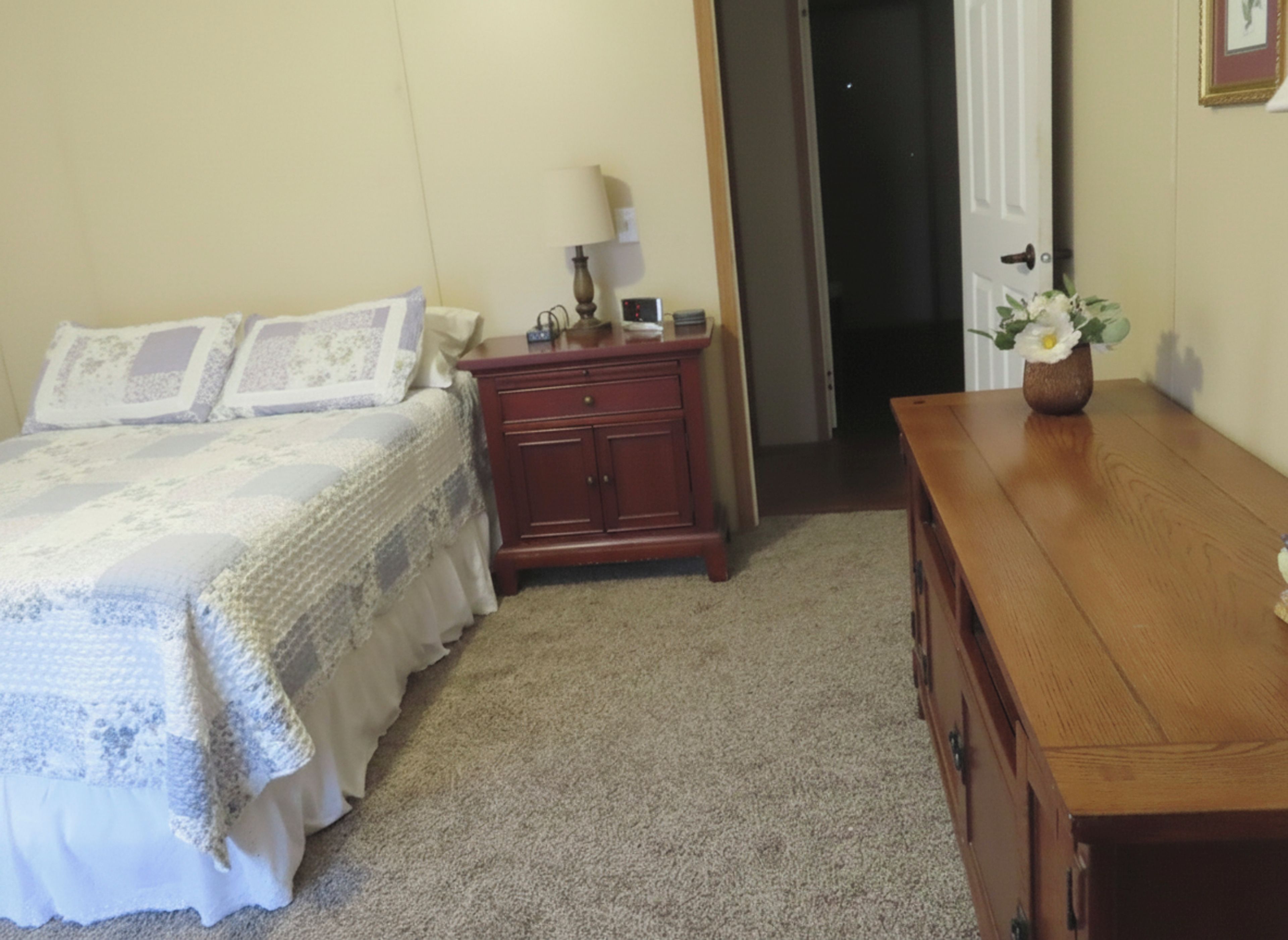 Un dormitorio con cama, cómoda, mesita de noche y un florero con flores.