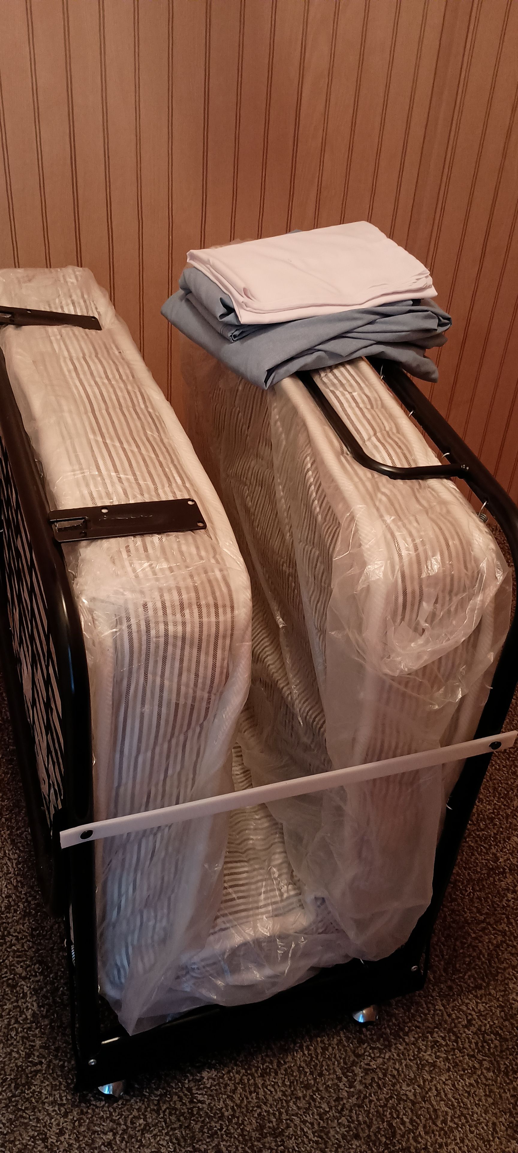 Un carrello nero per bagagli con due valigie avvolte nella plastica, una a righe e l'altra tinta unita.