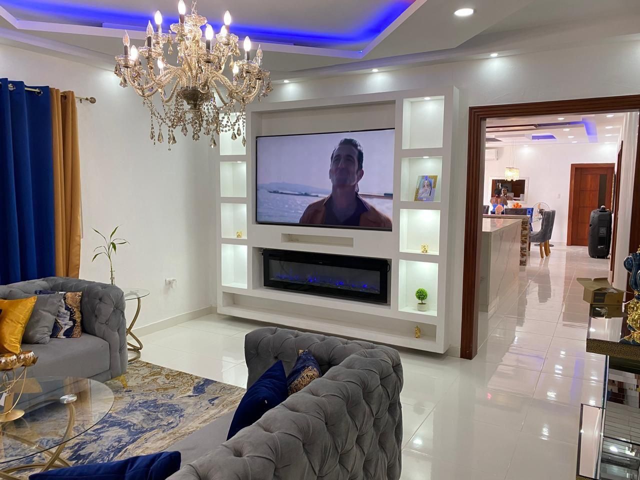 Un salon moderne avec un téléviseur à écran plat, un canapé gris, un lustre et un aquarium décoratif.