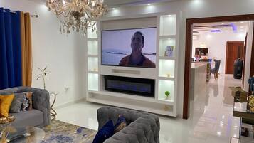 Un salon moderne avec un téléviseur à écran plat, un canapé gris, un lustre et un aquarium décoratif.
