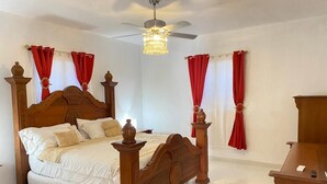 Une chambre à coucher avec un lit à baldaquin en bois, un ventilateur de plafond et des rideaux rouges.