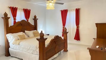 A bedroom with a wooden four-poster bed, a ceiling fan, and red curtains.